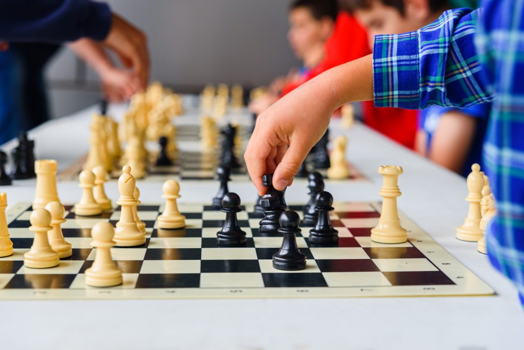 Child's hand moves the horse during a chess tournament with several game boards.